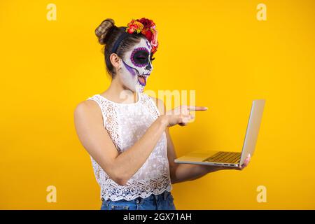 Catrina messicana, ritratto di giovane donna latina che tiene computer o laptop, festa di Halloween in Messico Foto Stock