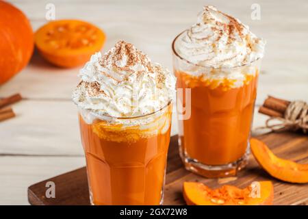 Latte piccante con zucca e panna montata su sfondo di legno. Caffè caldo in tazza di vetro e foglie d'autunno. Ricetta per frullati caldi. Foto Stock