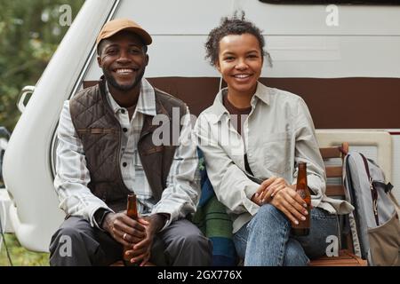 Ritratto di giovane coppia afroamericana rilassarsi all'aperto mentre campeggio con rimorchio furgone e guardare la macchina fotografica, spazio copia Foto Stock