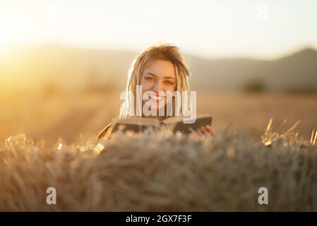 Bella e felice giovane donna che legge un libro su fieno balla Foto Stock