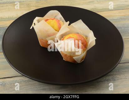 Due mini muffin alle fragole al limone in tazze di carta su piatto nero per la colazione Foto Stock