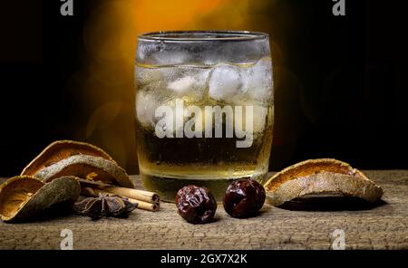 Succo di erbe e frutta in un bicchiere pieno di ghiaccio e frutta secca ed erbe secche poste su un vecchio tavolo di legno su sfondo bokeh sfocato. Foto Stock