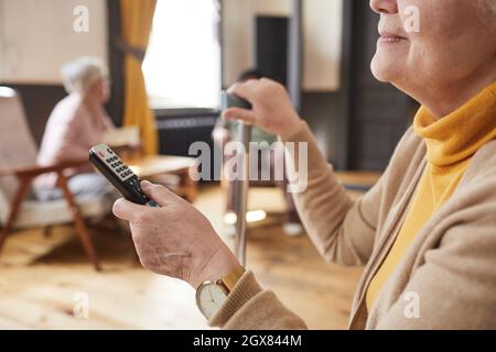 Primo piano della donna anziana caucasica che tiene il telecomando mentre guarda la TV in casa di cura, spazio copia Foto Stock