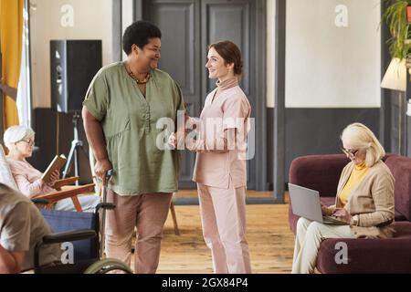 Ritratto di giovane donna sorridente che aiuta gli anziani nella casa di pensione moderna, spazio copia Foto Stock