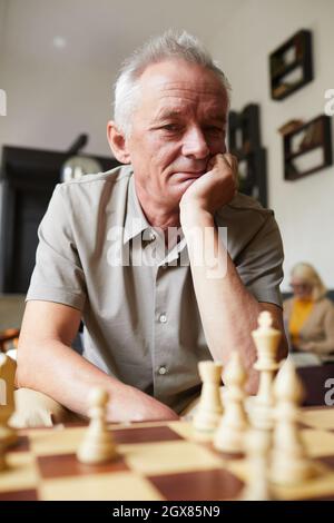 Ritratto verticale dell'anziano caucasico che gioca a scacchi e che si diverse in casa di cura Foto Stock