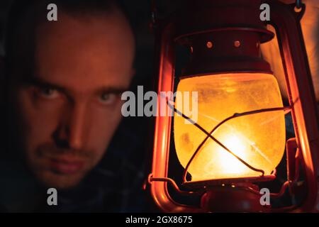 Una lampada a cherosene con fiamma arancione. Sullo sfondo c'è la faccia macchiata di un uomo Foto Stock