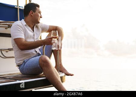 Giovane uomo che tiene un bicchiere di vino su un ponte aperto di una nave da crociera Foto Stock