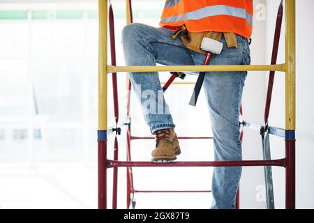 Giovane e bel costruttore che si arrampica su ponteggi in cantiere Foto Stock