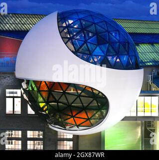 29 settembre 2021, Sassonia, Lipsia: Dopo il tramonto, la sfera illuminata Niemeyer sorge dal cielo blu sopra gli edifici del costruttore di gru Kirow e del costruttore di tram HeiterBlick sui terreni di 'Techne Sphere Leipzig' durante una serata di menu. La sfera di cemento e vetro di 12 metri, progettata dall'architetto brasiliano Oscar Niemeyer (1907-2012), completata nell'estate del 2020, ospita ora le sue prime celebrazioni ed eventi dopo la lunga pausa di Corona. La struttura a cupola con i suoi tre livelli e circa 150 triangoli di vetro in cima ad un edificio industriale in mattoni è la Foto Stock