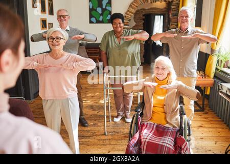 Gruppo di persone anziane sorridenti che godono di esercizi mattutini in casa di riposo, spazio copia Foto Stock