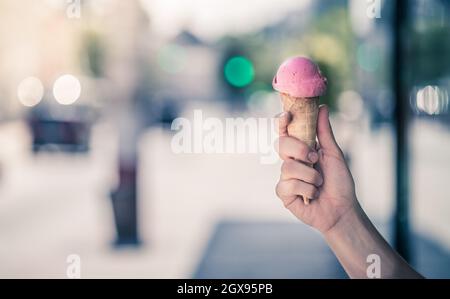 Donna detiene il gelato alla fragola in mano, soleggiata giornata estiva, sfondo sfocato Foto Stock