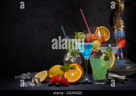 Set di hookah e cocktail. Bicchieri con varie bevande fredde, frutta, narghilè e utensili da bar su sfondo grigio scuro. Fine settimana o festa di vacanza. Hookah Foto Stock