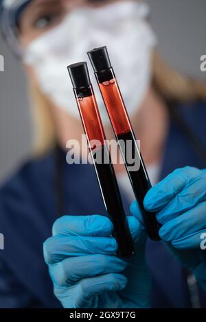 L'Operaio Di Laboratorio Femminile Che Indossa La Maschera Medica Per Il Viso Può Contenere Provette Di Sangue Contro Sfondo Scuro. Foto Stock