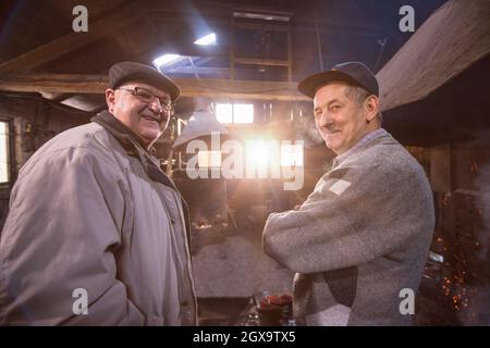 Ritratto di due fiducioso fabbro senior in piedi con le braccia conserte nel workshop tradizionali Foto Stock