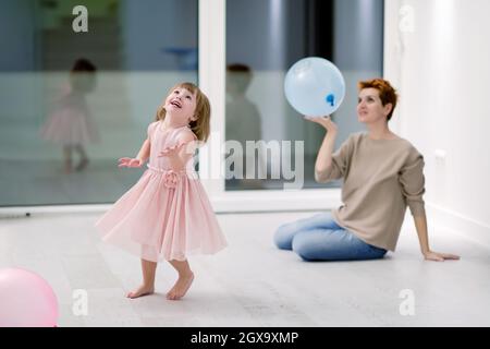 la famiglia felice che trascorre il tempo insieme giovane madre redhead e figlia piccola cute che si divertono mentre gioca con i palloncini vicino alla finestra su bello Foto Stock