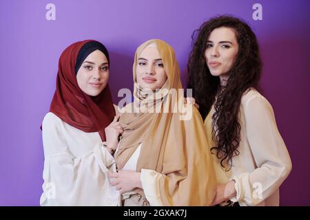 ritratto di gruppo di belle donne musulmane due di loro in abito alla moda con hijab isolato su sfondo viola che rappresenta la moda moderna islam a. Foto Stock