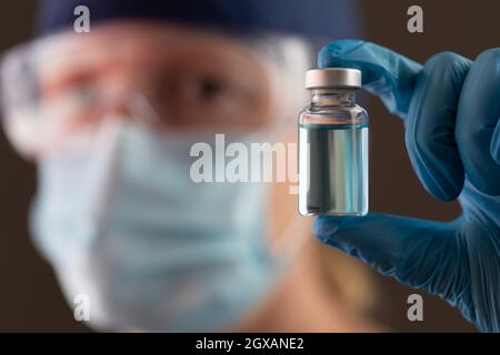 Femmina di lavoro medico che tiene il flaconcino del vaccino che indossa la maschera protettiva del viso e gli occhiali di protezione. Foto Stock