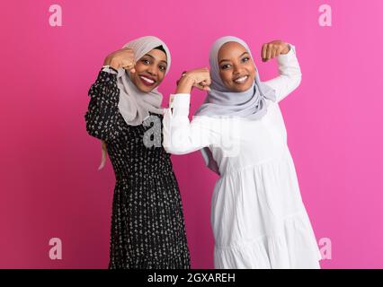 due ragazze africane che indossano abiti islamici tradizionali su sfondo rosa di plastica che mostrano forza e parità di genere di potere Foto Stock