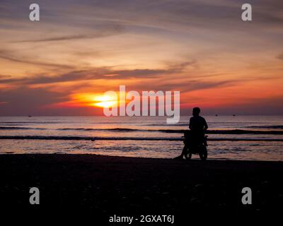 Turisti asiatici maschi da silhouette moto in mare Foto Stock