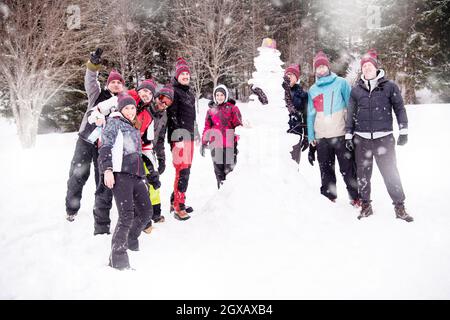 Ritratto di gruppo di giovani happy business persone dopo un concorso in posa con finito di pupazzo di neve mentre godendo nevoso inverno giornata con i fiocchi di neve intorno Foto Stock