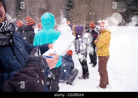 Gruppo di giovani happy business persone dopo un concorso la misura di altezza finita del pupazzo di neve mentre godendo nevoso inverno giornata con i fiocchi di neve arou Foto Stock