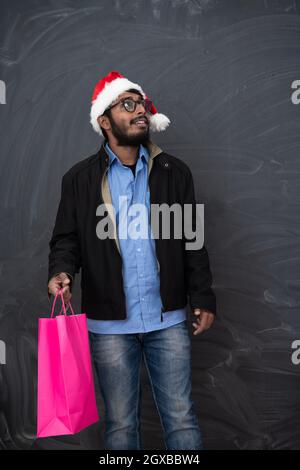 Indian uomo che indossa abiti di festa di Santa hat con shopping bag su sfondo scuro studio dark scuoiati Middle Eastern Santa Claus Buon Natale Foto Stock