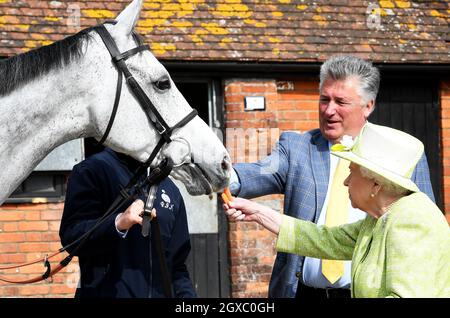 La regina Elisabetta II nutre una carota ad un cavallo, guardato dall'addestratore Paul Nicholls, durante una visita alle scuderie della fattoria del Maniero a Ditcheat, Somerset il 28 marzo 2019. Foto Stock