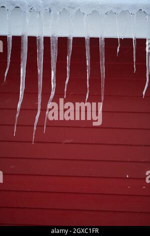 Ghiacci sul tetto di una casa rossa in Norvegia. Sciogliendo ghiacci. Formazione di ghiaccio naturale in inverno. Foto Stock