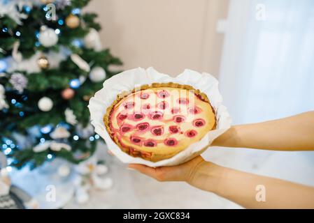 Torta di ciliegia al forno in mano sullo sfondo dell'albero di Natale Foto Stock