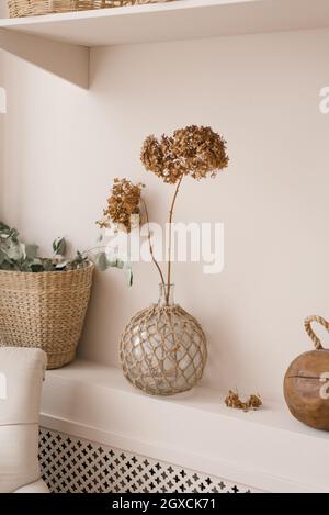 Decorazioni scandinave come decorazione nella casa. Fiori essiccati di hydrangea in un vaso, rami di eucalipto in un cestino di vimini su una mensola nel roro vivente Foto Stock