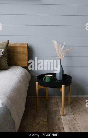 Un vaso di fiori secchi e una tazza sul comodino in stile scandinavo in camera da letto. Foto Stock