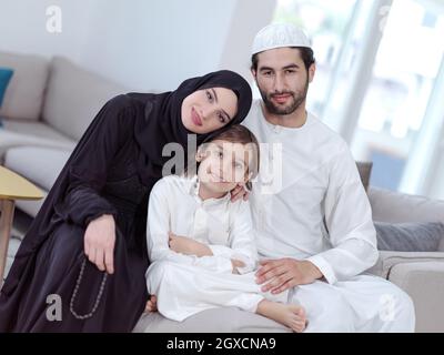 I genitori tradizionali della famiglia musulmana con i bambini che leggono il Corano e pregano insieme sul divano prima della cena di iftar durante una festa del ramadan a casa Foto Stock