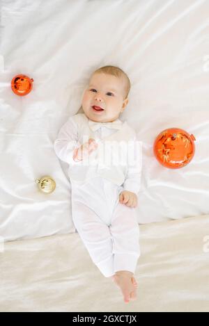 Il bambino è sdraiato sul letto nella camera da letto circondato da palline di giocattoli albero di Natale e ridendo Foto Stock