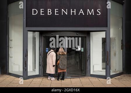 Due donne guardano dentro attraverso la porta di vetro del negozio chiuso e vuoto Debenhams in Princes Street, Edimburgo, Scozia, Regno Unito. Foto Stock