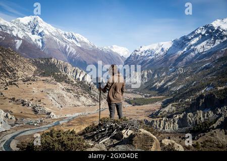 Vista posteriore di un esploratore irriconoscibile con capelli volanti in piedi su pendio roccioso e ammirando il pittoresco scenario della catena montuosa in Nepal Foto Stock