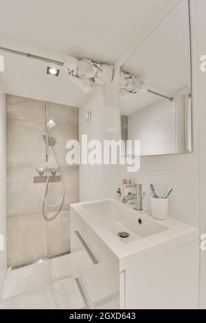 Moderno bagno interno con lavabo in ceramica sotto specchio contro la doccia camera con lampada in casa Foto Stock