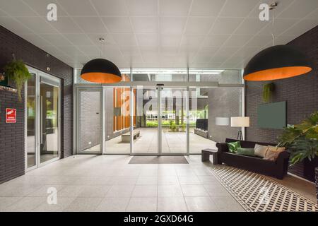 Interni moderni con cuscini sul divano e lampade appese tra le pareti in mattoni durante il giorno Foto Stock