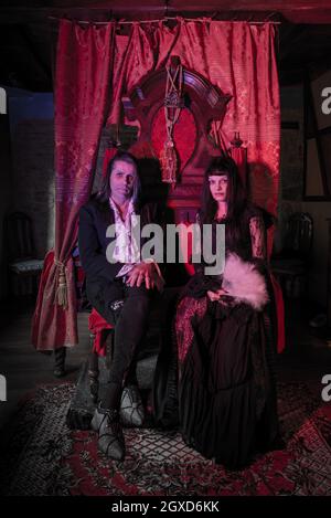 uomo e donna in abiti gotici seduti su un trono in un ambiente medievale. Vampiri. Foto Stock