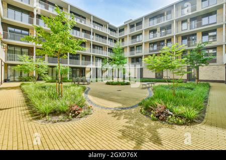 Passerella in mattoni che passa tra alberi verdi e piante nel cortile interno di un moderno edificio condominio Foto Stock