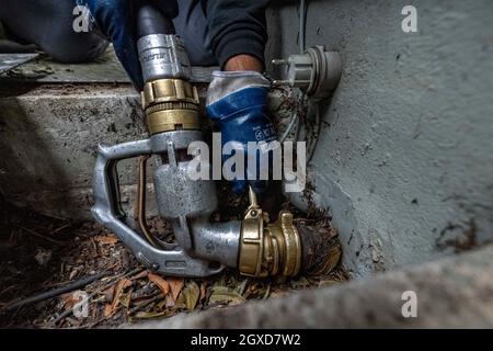 Lippstadt, Germania. 05 ottobre 2021. Un dipendente avvita il tubo flessibile per l'erogazione dell'olio di riscaldamento sul raccordo dell'abitazione. I consumatori possono aspettarsi un forte aumento dei costi di riscaldamento quest'anno a causa dell'elevata domanda globale di petrolio greggio. Sarà ancora più costoso in 2021 nelle case con il riscaldamento di petrolio, dove i costi sono previsti aumentare del 44 per cento - dopo un calo del 27 per cento nell'anno precedente. Credit: David Inderlied/dpa/Alamy Live News Foto Stock