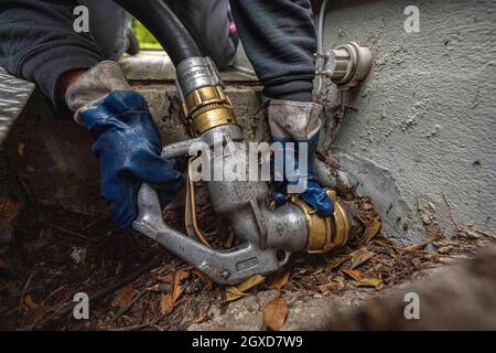 Lippstadt, Germania. 05 ottobre 2021. Un dipendente avvita il tubo flessibile per l'erogazione dell'olio di riscaldamento sul raccordo dell'abitazione. I consumatori possono aspettarsi un forte aumento dei costi di riscaldamento quest'anno a causa dell'elevata domanda globale di petrolio greggio. Sarà ancora più costoso in 2021 nelle case con il riscaldamento di petrolio, dove i costi sono previsti aumentare del 44 per cento - dopo un calo del 27 per cento nell'anno precedente. Credit: David Inderlied/dpa/Alamy Live News Foto Stock