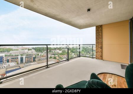 Comoda poltrona e tavolo collocati su un ampio balcone con recinzione in vetro in luce naturale Foto Stock