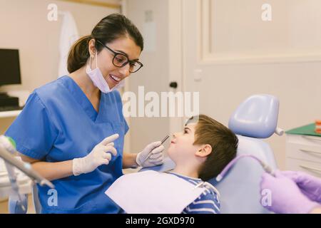 ragazzo che parla con i medici durante il trattamento dentale in studio dentistico contemporaneo Foto Stock