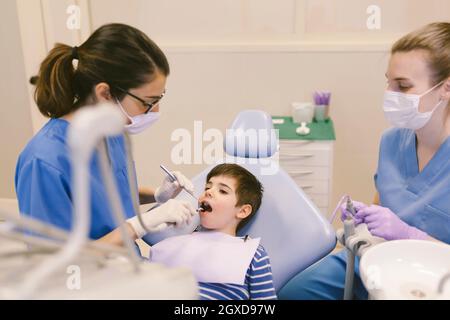 Alto angolo di dentista e assistente che tratta i denti del ragazzo durante la procedura in clinica di odontoiatria Foto Stock