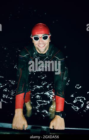 un vero nuotatore triatleta che ha una pausa durante l'allenamento al lago durante la notte buia Foto Stock