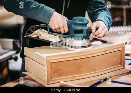 dettaglio di un falegname con una levigatrice orbitale. Foto Stock