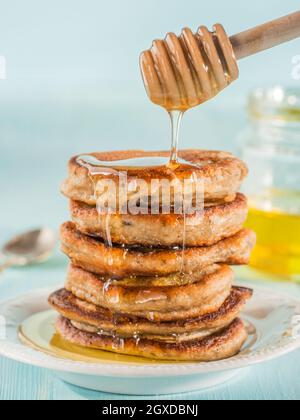 Pila di piccole pancake con banana e semi di chia nel miele su fondo azzurro. Il miele di versarla sulla pila di mini pancake con chia o di papavero, vedere Foto Stock