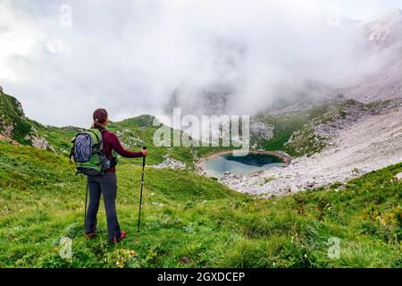 Donna escursionista che gode di una fantastica vista di un lago di montagna avvolto da nuvole Foto Stock