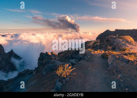 Alba su un sentiero di montagna ad alta quota tra morbide e spesse nuvole bianche e l'eruzione di un vulcano sullo sfondo. Cumbre Vieja eruzione vulcanica Foto Stock