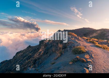 Alba su un sentiero di montagna ad alta quota tra morbide e spesse nuvole bianche e l'eruzione di un vulcano sullo sfondo. Cumbre Vieja eruzione vulcanica Foto Stock